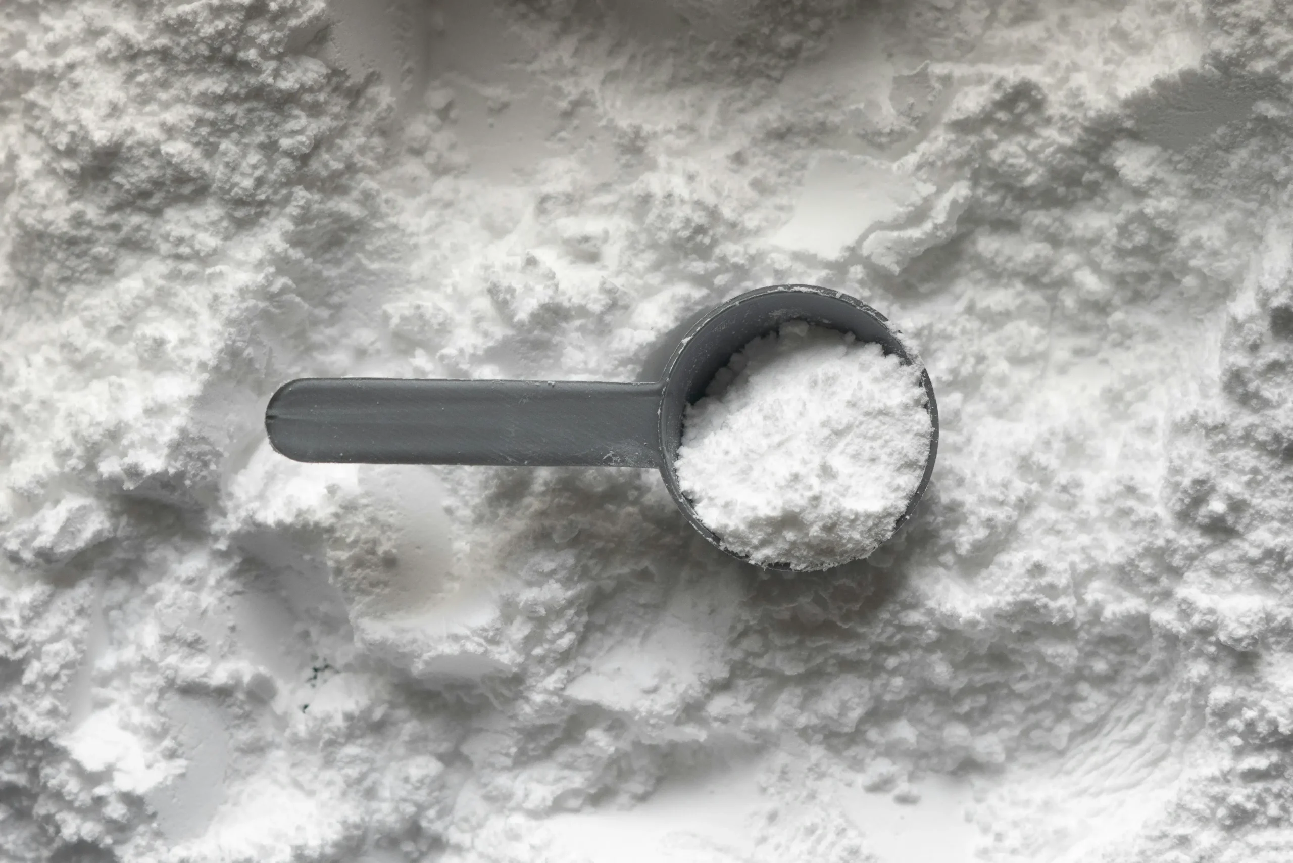 Pote de creatina em pó sobre uma mesa, suplemento usado para ganho de força muscular